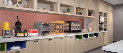 Een moderne keuken met houten kastjes, een koffieapparaat, een broodvitrine en diverse keukengerei.