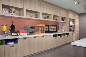 Un área de cocina moderna con armarios de madera, una cafetera, un expositor para pan y diversos utensilios de cocina.