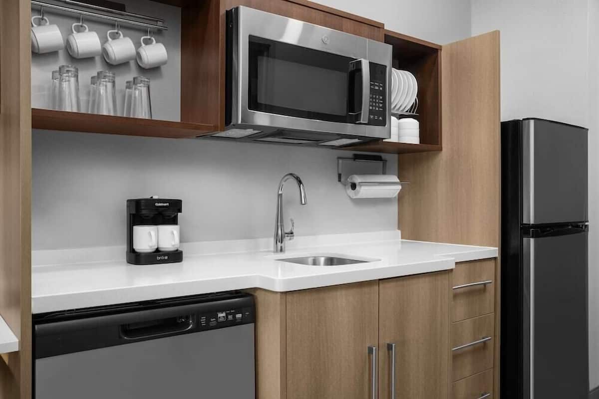 Una cocina moderna con microondas integrado, cafetera, lavavajillas y refrigerador de acero inoxidable.