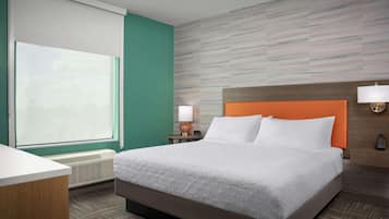 A hotel room with a large bed, a desk, a window with blinds, a wall-mounted lamp, and a heater.