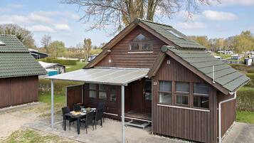 A wooden cabin with a covered patio, a dining area, and a small porch.