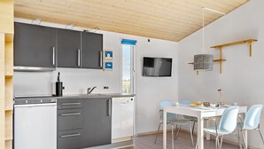 A modern kitchen with grey cabinets, a white dishwasher, and a dining area with a white table and blue chairs. - First Camp Frigard   Flensborg Fjord (Krusaa)