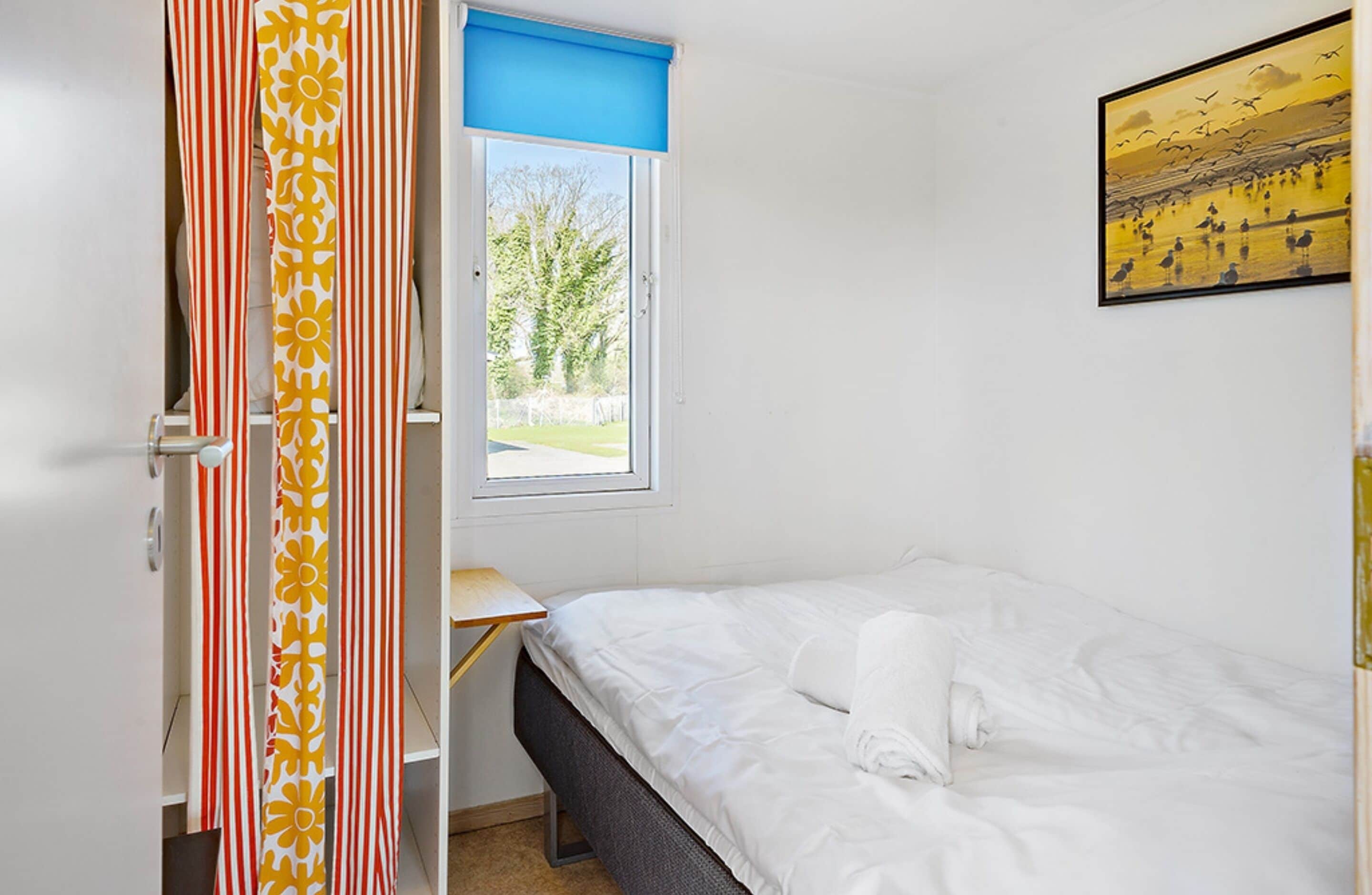 A bedroom with a bed, a window with a view of trees, and a painting on the wall.