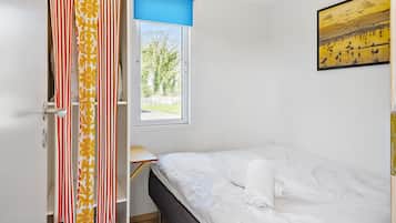 A bedroom with a bed, a window with a view of trees, and a painting on the wall.