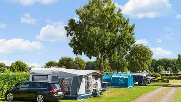 Ein Campingplatz mit mehreren Zelten und einem Wohnwagen, einem Feldweg und einem großen Baum im Hintergrund.