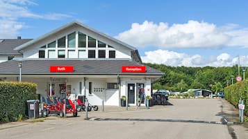 A building with 'Butik' and 'Reception' signs, a parking area with bicycles, and a clear sky.