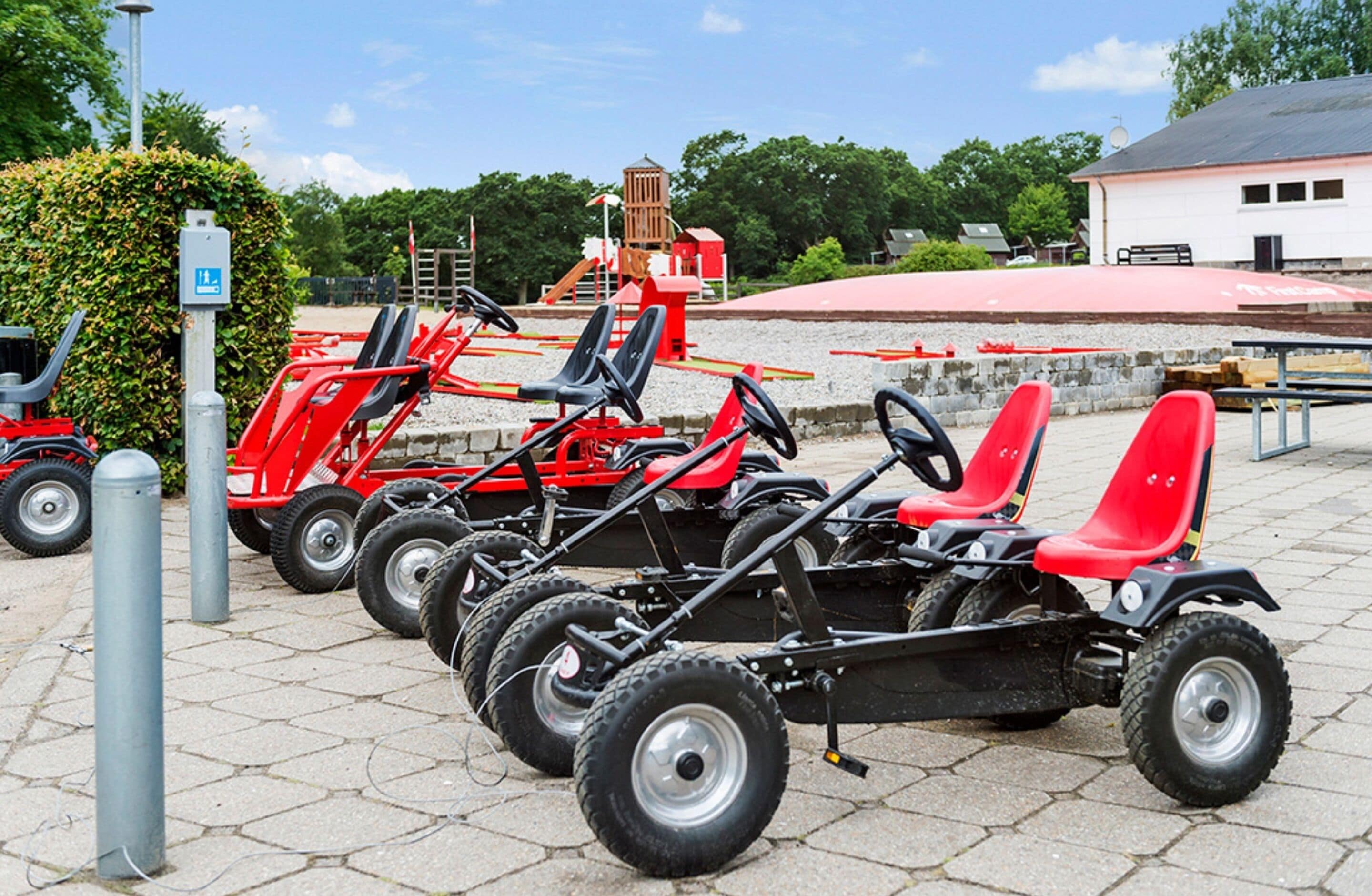 A row of red go-karts parked on a paved area with a building and trees in the background.