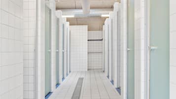 A clean, tiled restroom corridor with multiple stalls, a ventilation system, and a drain in the center.