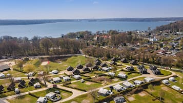 Vista aérea de un camping con vehículos recreativos y casas móviles, rodeado de árboles y un lago.