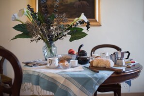 A dining table with a vase of flowers, a teapot, a croissant, and a bowl of fruit. - Italian Experience - Duomo Suite (Florence)