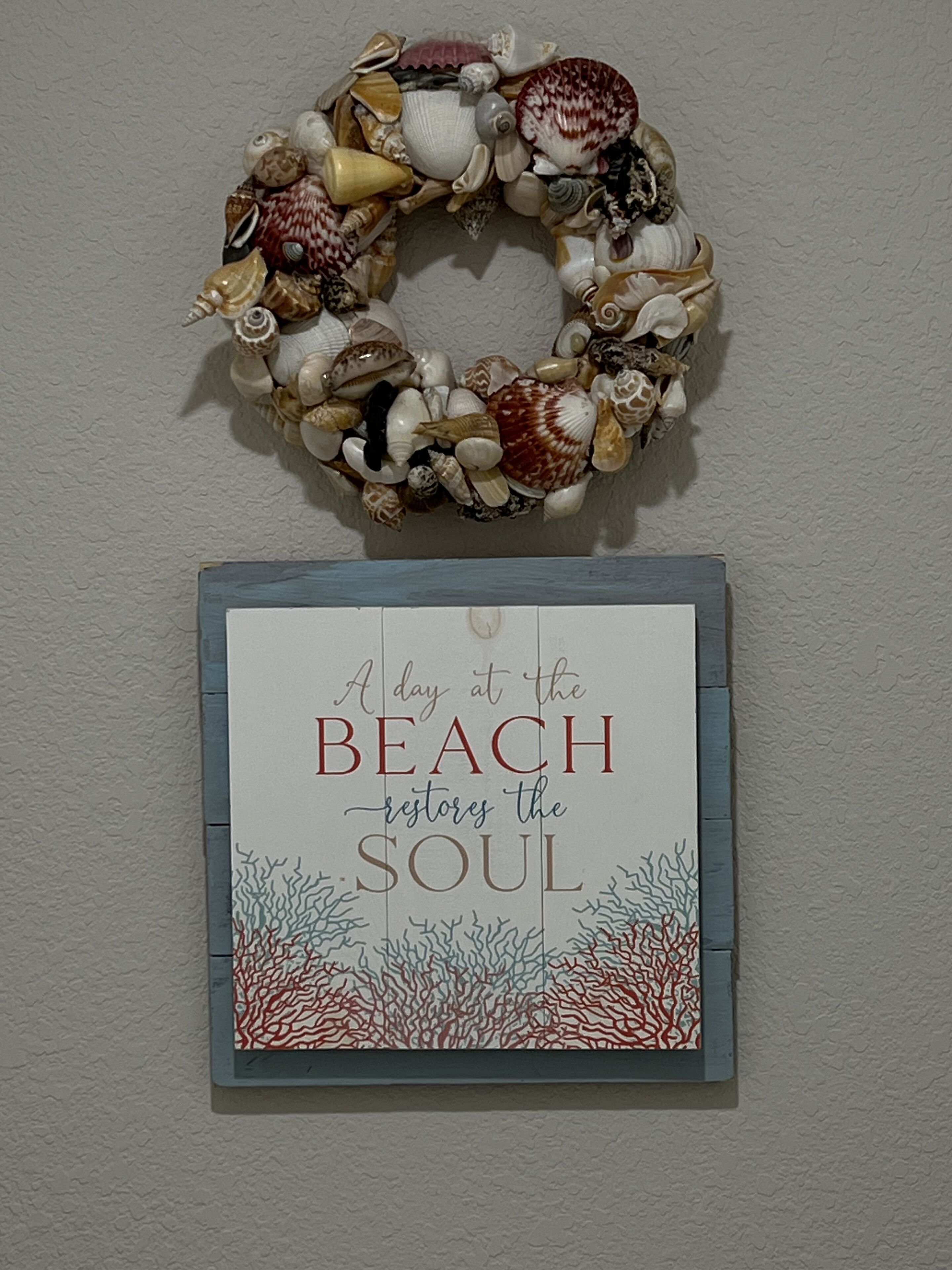 Decoração de parede com uma placa com tema de praia que diz 'Um dia na praia renova a alma'.