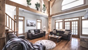 A spacious living room with wooden beams, leather sofas, a round rug, and large windows. - Luxury Chalet in the Woods w/ Pool & Hot Tub, Near Wasaga Beach & Blue Mountain! (Minesing)