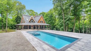 A house with a swimming pool surrounded by a wooden deck and trees. - Luxury Chalet in the Woods w/ Pool & Hot Tub, Near Wasaga Beach & Blue Mountain! (Minesing)