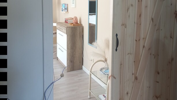 Habitació amb armari de fusta, mirall, taula petita amb llibres i una cadira.