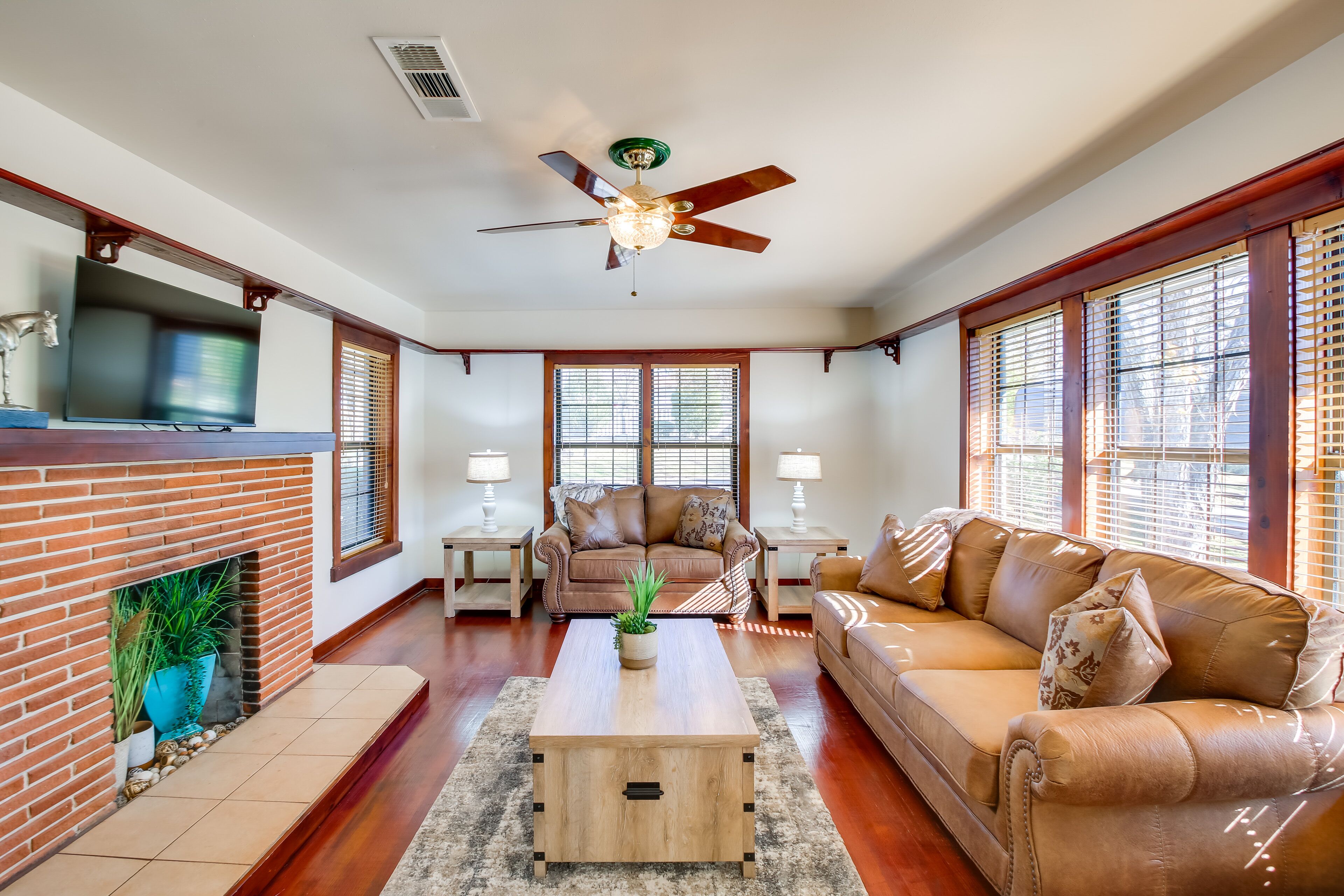 A living room with a fireplace, a ceiling fan, a television, and two couches.