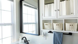 A bathroom with a white sink, a black faucet, a mirror, and a towel rack with a blue towel. There are wicker baskets on a shelf above the towel rack.
