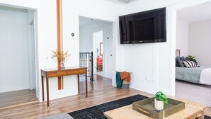 A modern living room with a wooden coffee table, a TV mounted on the wall, and a staircase leading to another room.