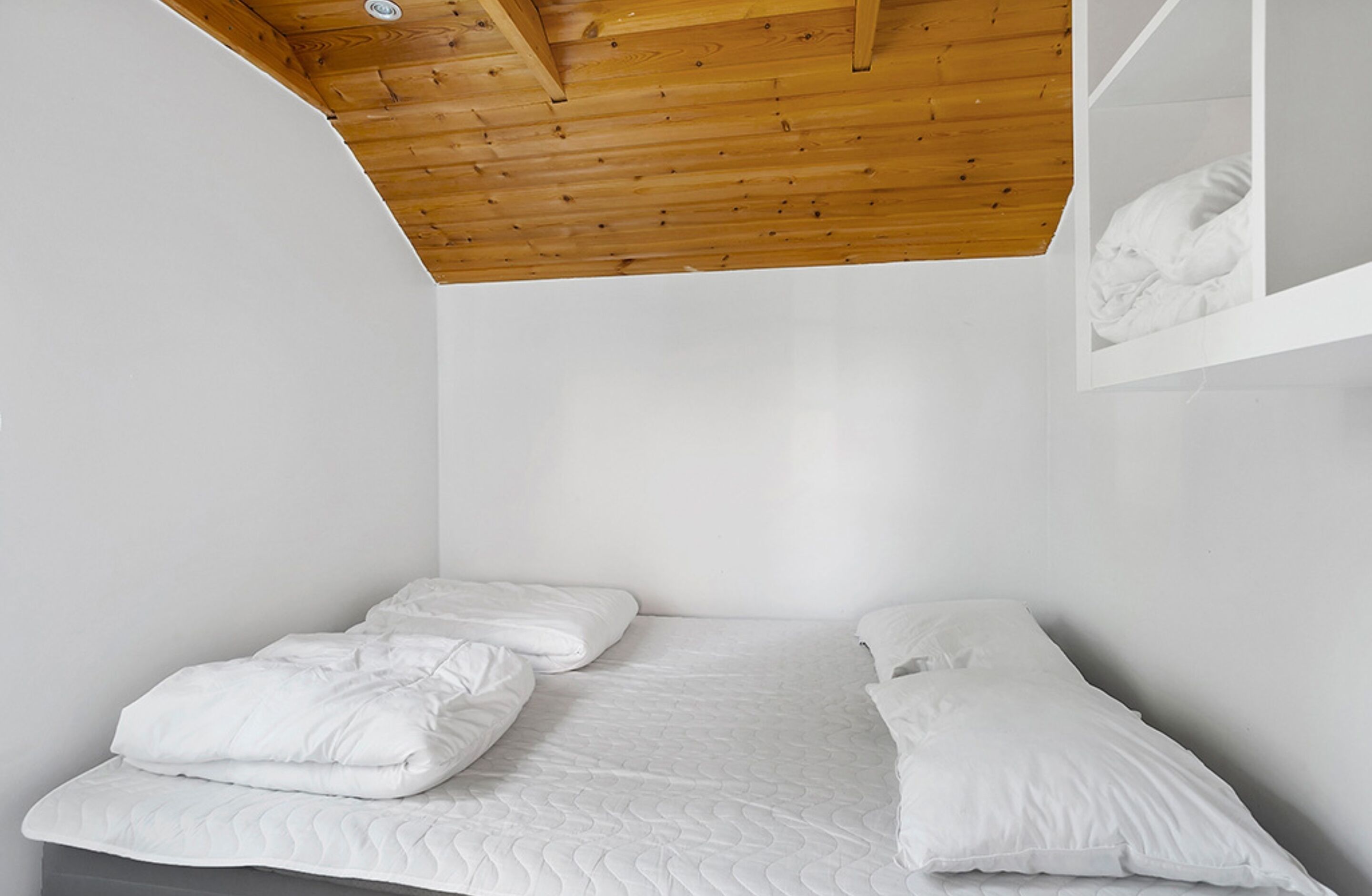 A small, white, single-bed room with a wooden ceiling and a white wall.