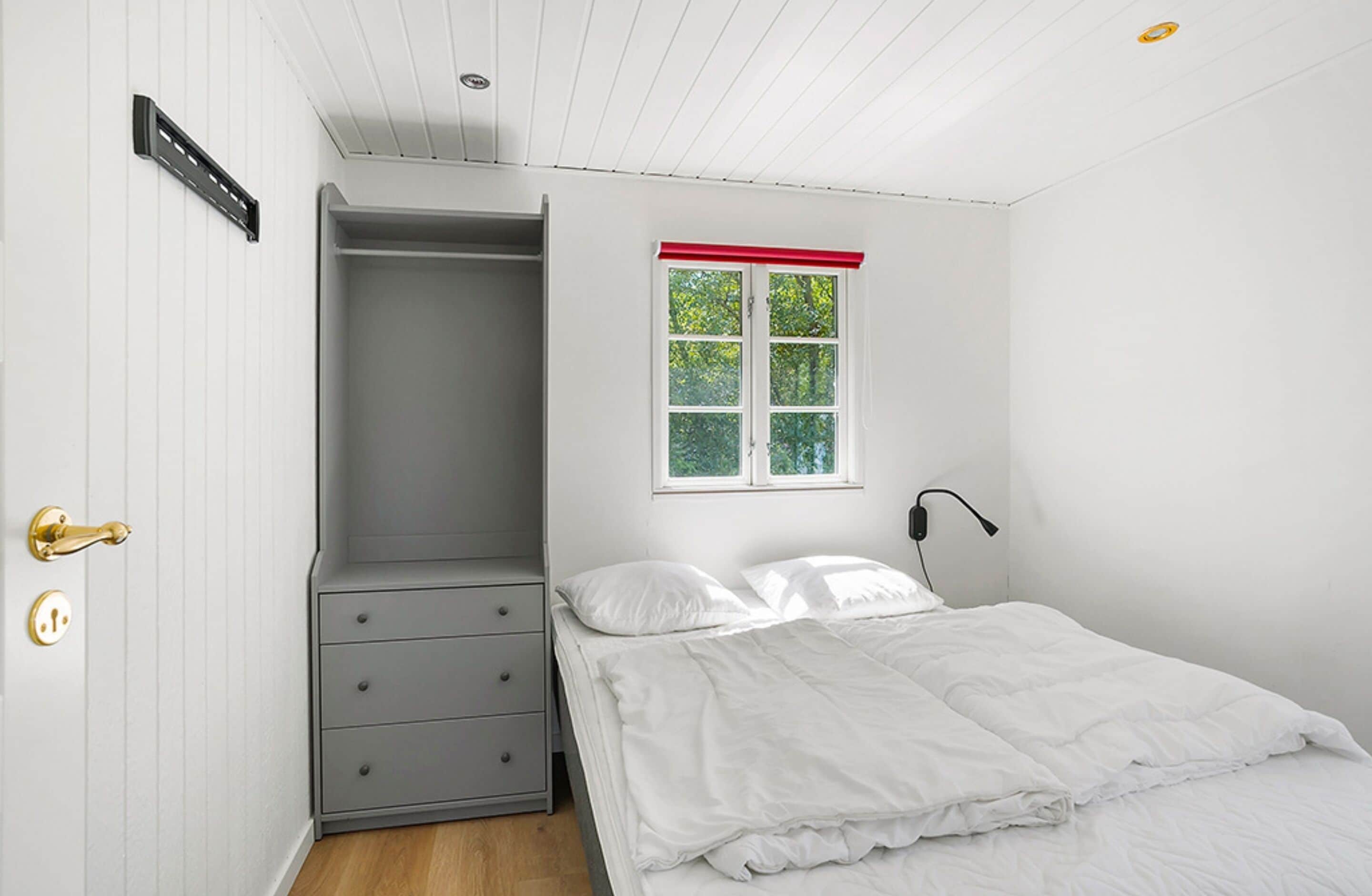 A bedroom with a bed, a wardrobe, a window, and a door with a lock.