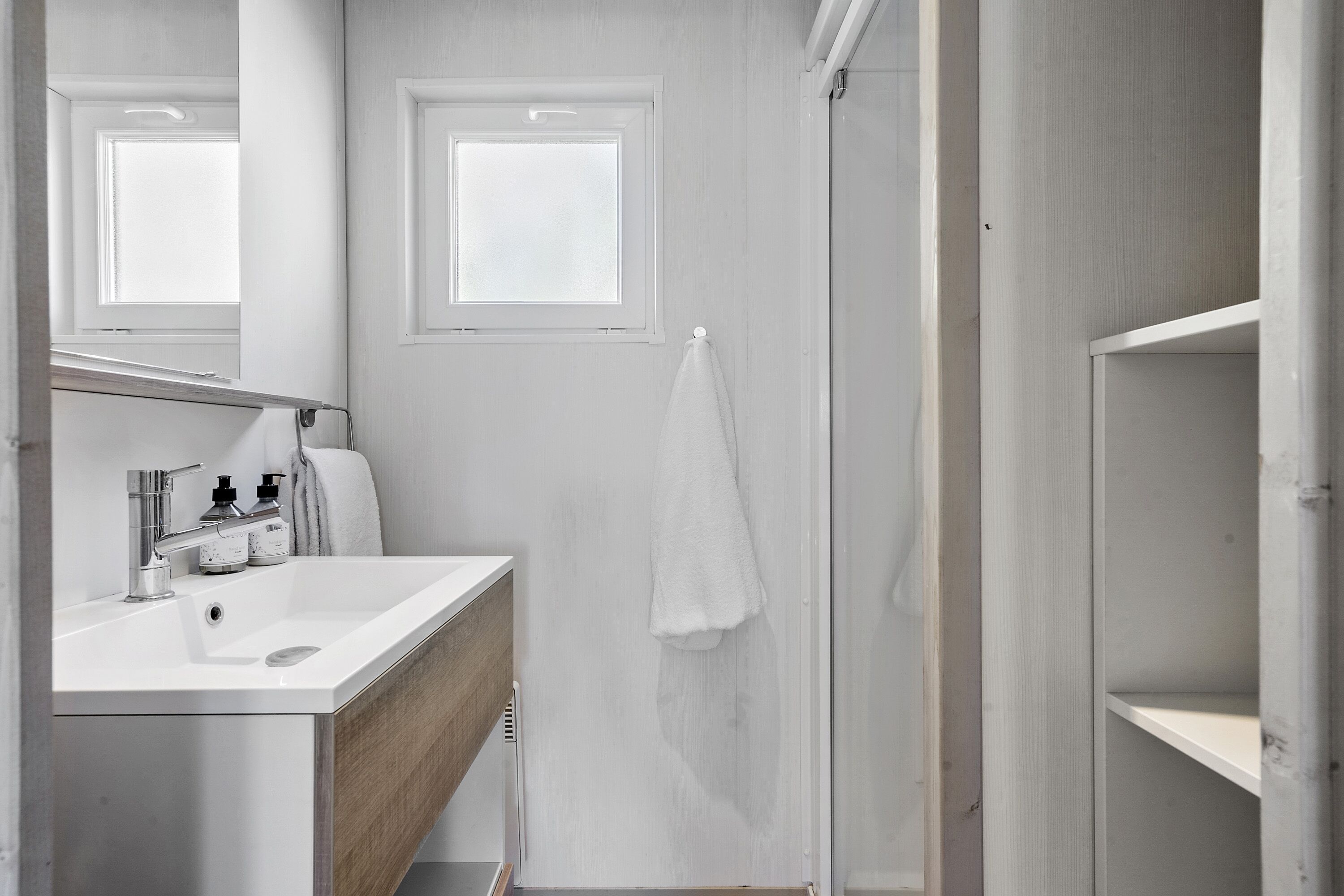 Une salle de bain moderne avec un lavabo blanc, un miroir et deux fenêtres.