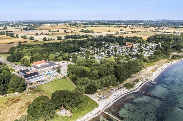 Vue aérienne d’une zone côtière comprenant un port de plaisance, un grand bâtiment doté d’un toit rouge et un ensemble dense de tentes blanches.