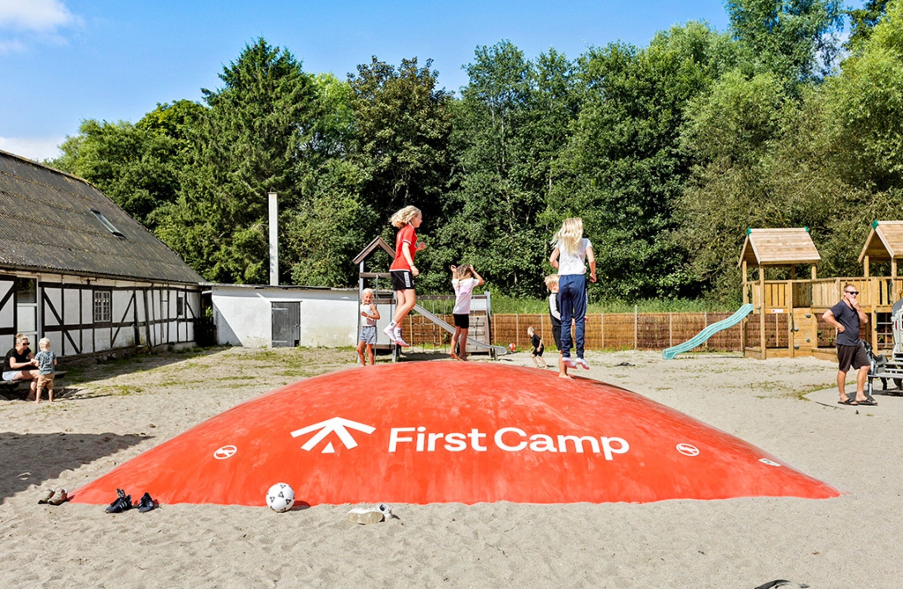 A sandy area with a red mat labeled "First Camp" and a playground with wooden play structures.