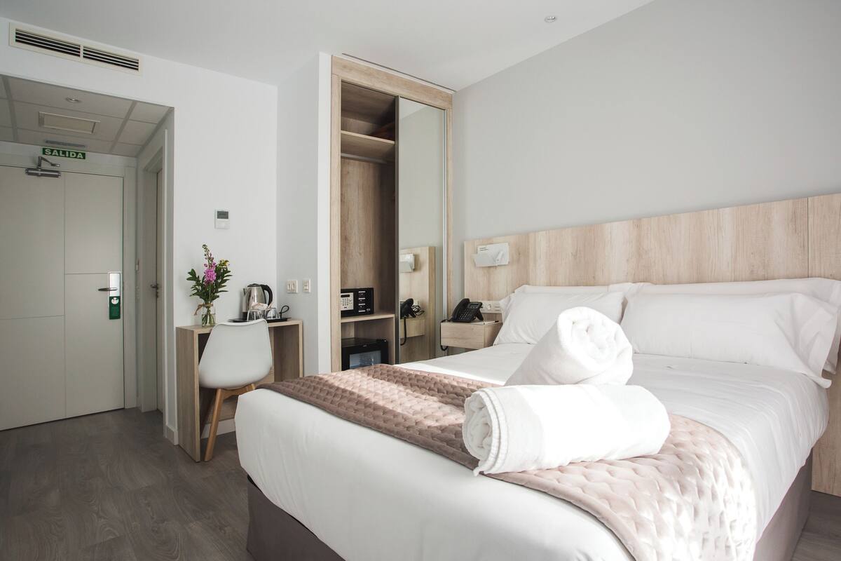 A hotel room with a bed, a desk, a chair, a mirror, a wardrobe, and a bathroom.