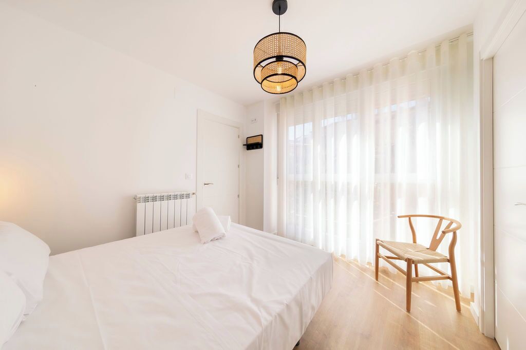 A bedroom with a bed, a chair, a radiator, and a window with curtains.