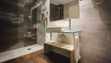 Un baño moderno con cabina de ducha de vidrio, lavamanos con tapa de cristal y un banco.