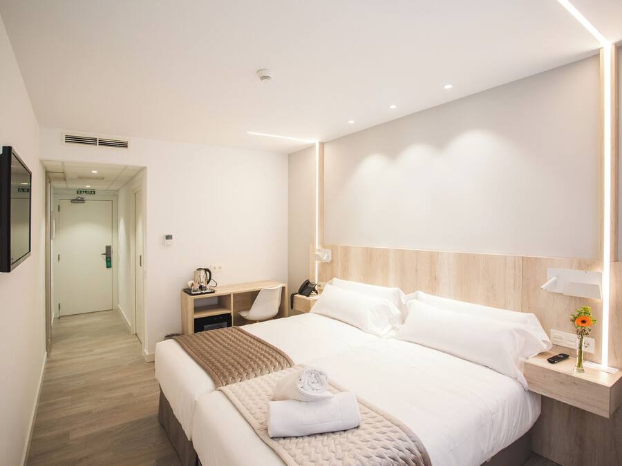 Una camera d'albergo moderna con un letto rifatto, un comodino con una lampada, un telefono e un piccolo vaso con un fiore.
