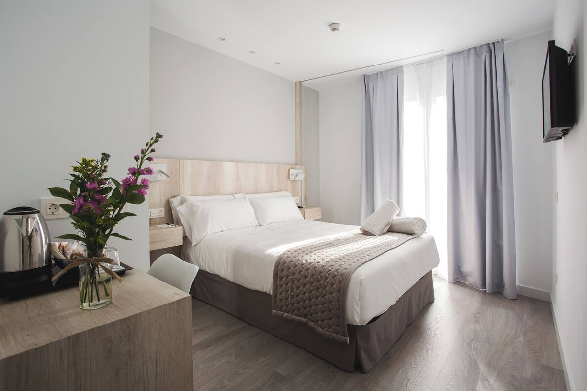 A modern hotel room with a bed, bedside table, and a vase of flowers.