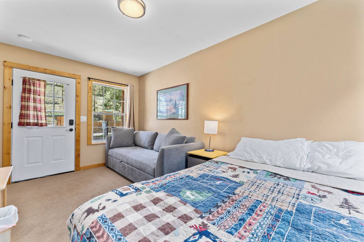 A bedroom with a bed, a couch, a nightstand, a door, and windows.