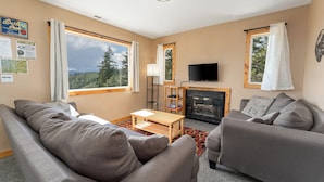 A cozy living room with a fireplace, large windows, and a flat-screen TV. - Echo Valley Resort & Cabins (Manson)