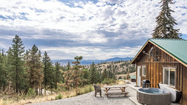 A wooden cabin with a hot tub, a picnic table, and a fire pit, surrounded by trees and mountains. - Echo Valley Resort & Cabins (Manson)