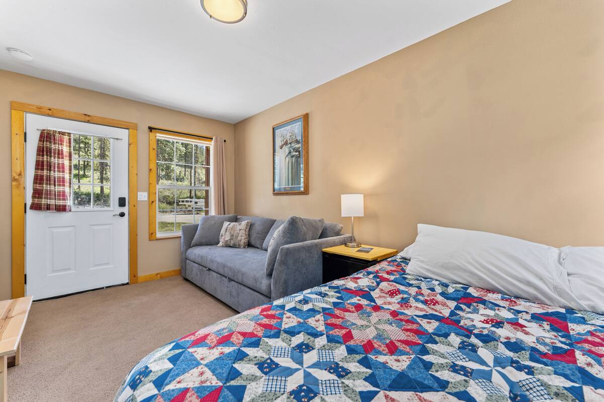 A bedroom with a bed, a sofa, a door, and windows.