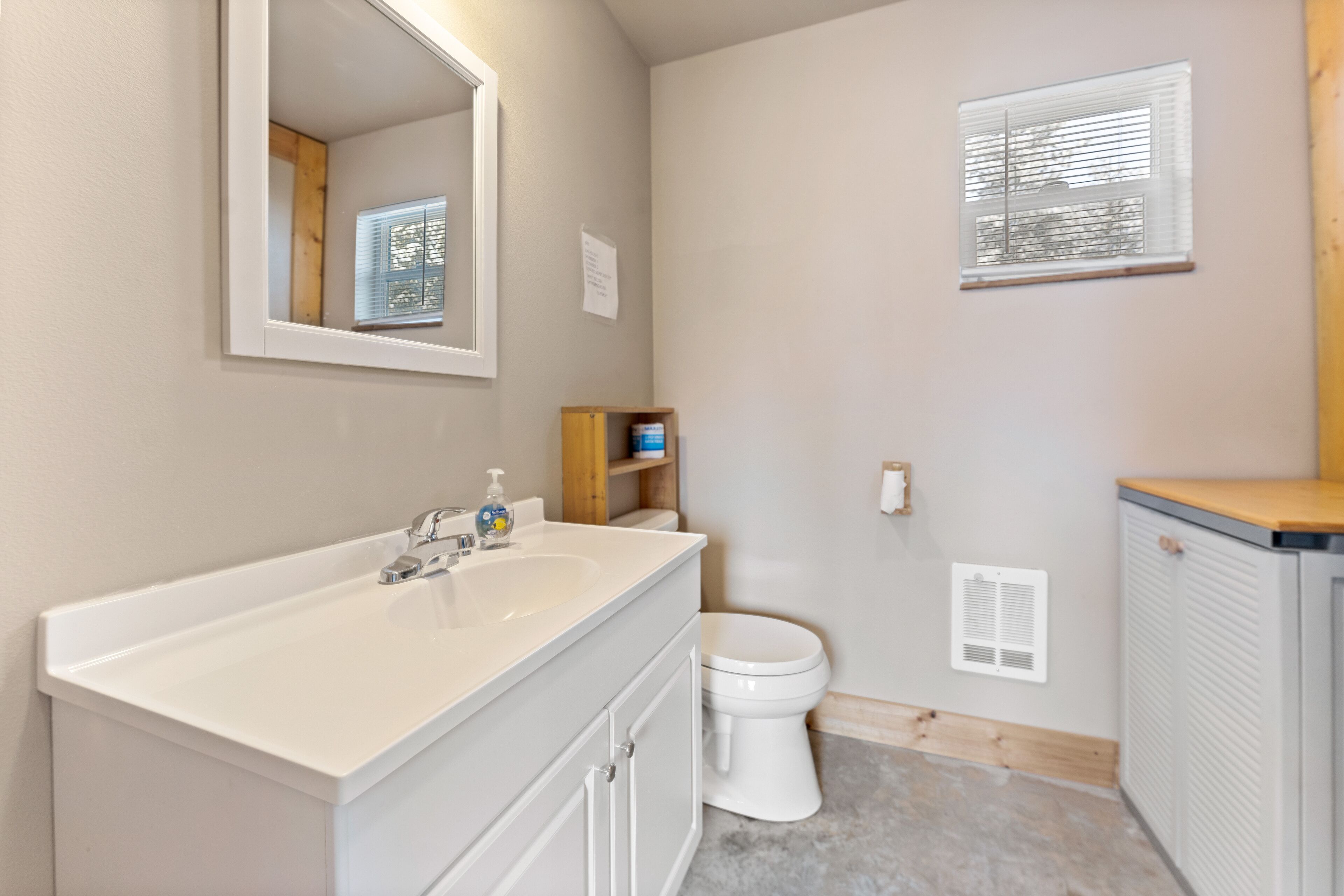 A bathroom with a white sink, mirror, toilet, and a window with blinds.