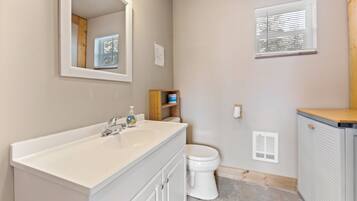 A bathroom with a white sink, mirror, toilet, and a window with blinds.