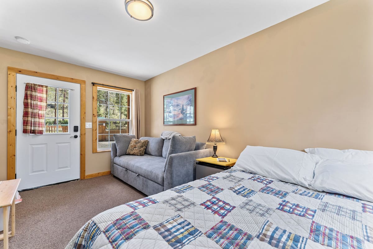 A bedroom with a bed, a sofa, a desk, and two windows.