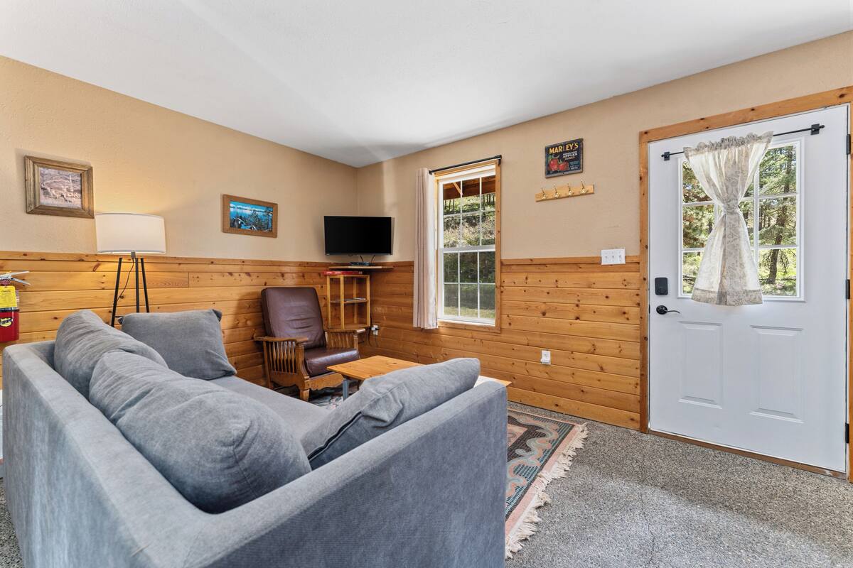 A cozy room with a grey sofa, a wooden chair, a small table, a television, and a door with a window.