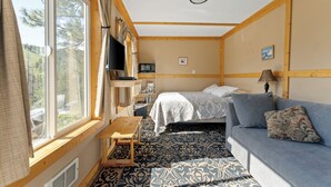 A cabin with a bed, a sofa, a TV, a table, and a window with curtains. - Echo Valley Resort & Cabins (Manson)