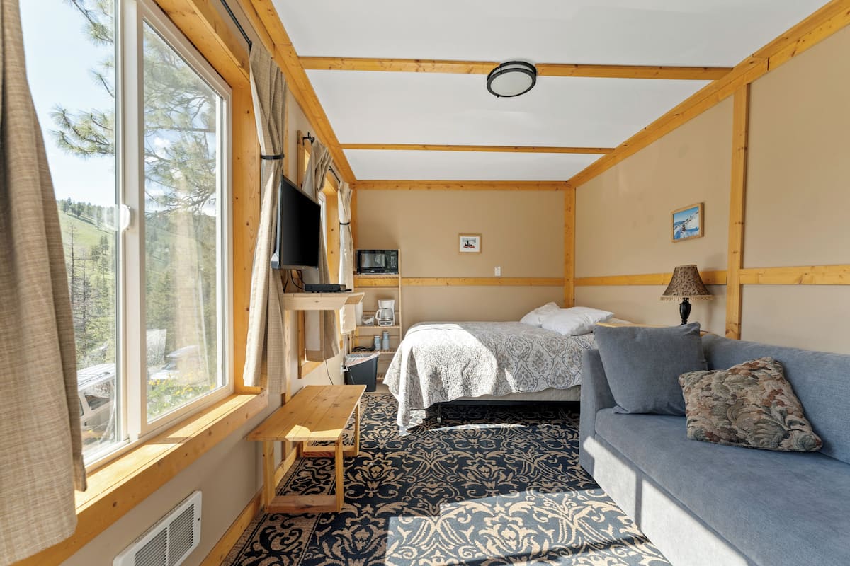 A cabin with a bed, a sofa, a TV, a table, and a window with curtains.
