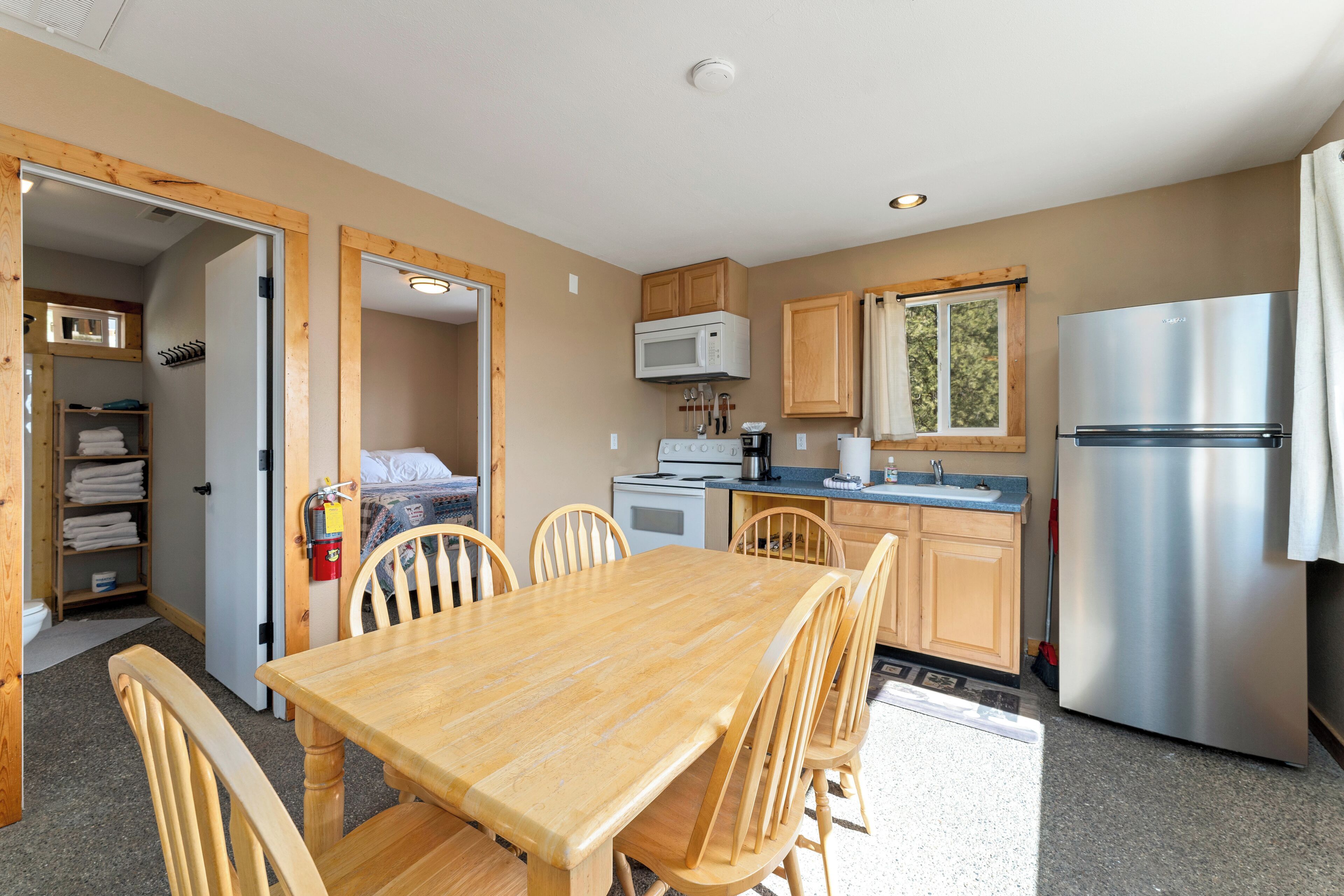 A compact kitchen with wooden cabinets, a stainless steel refrigerator, and a dining area with a wooden table and chairs.