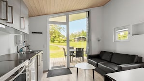 Una cocina moderna con horno empotrado, una zona de comedor con mesa y sillas, un sofá de cuero negro y un ventanal corredero que da a un patio con mobiliario exterior.