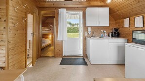 Una cabaña de madera acogedora con kitchenette, una cama y una puerta que da a un jardín.