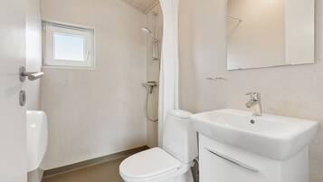 A bathroom with a toilet, sink, shower, and a window.