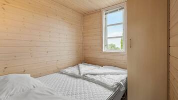 A small, wooden-paneled room with a single bed, a window, and a door.