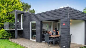 A modern black house with a deck, a balcony, and a dining area with a table and chairs. - First Camp Skovlund  Lillebælt (Middelfart)