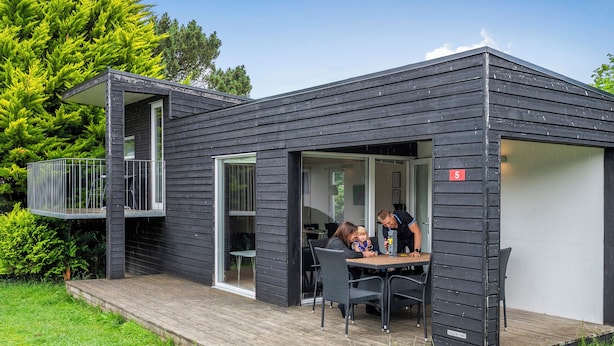 Una casa moderna negra con una terraza, un balcón y un comedor con mesa y sillas.