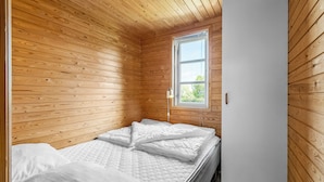 Una habitación pequeña con paneles de madera, una cama individual, una ventana y una puerta.