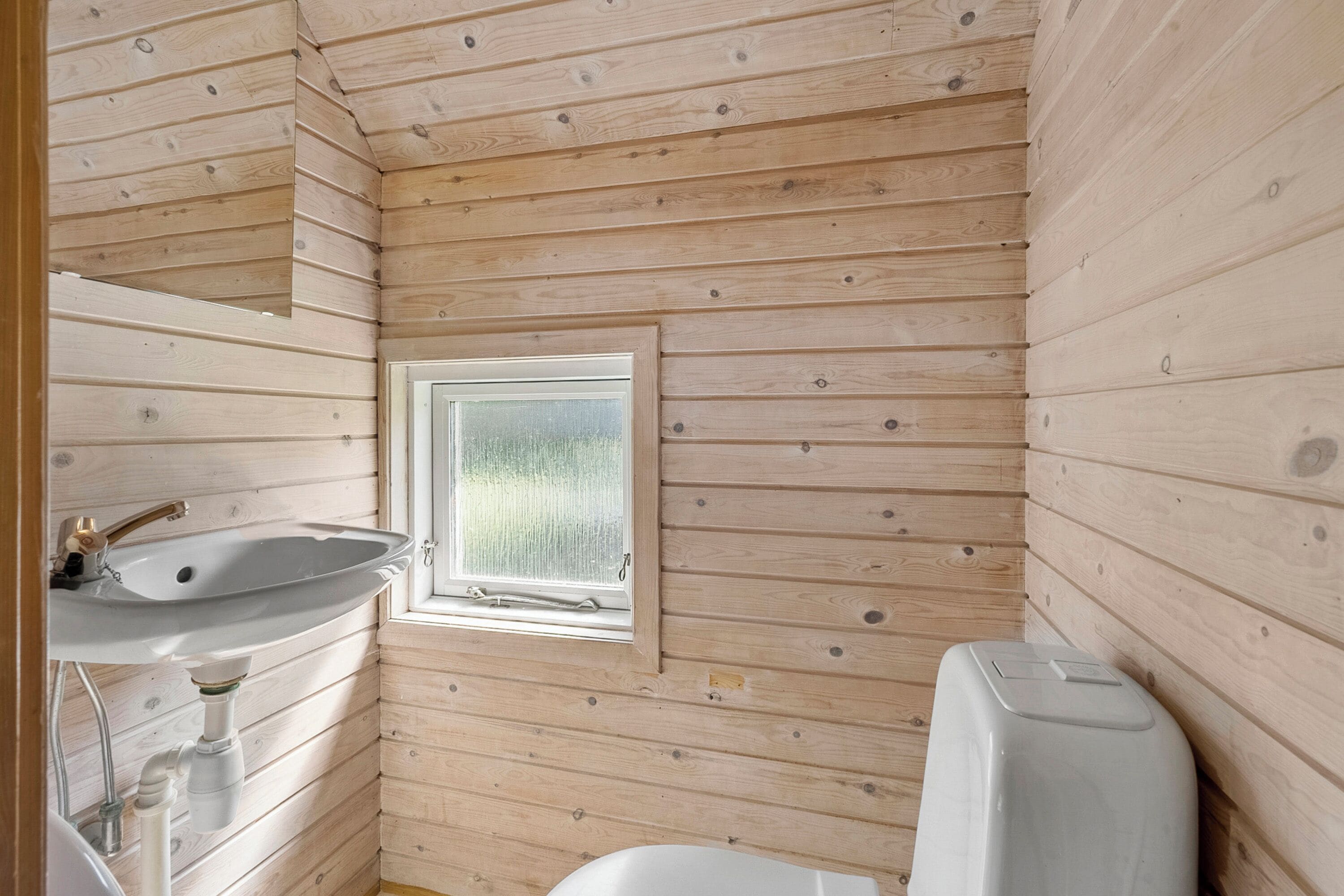Bagno di una baita in legno con lavandino, finestra e WC.